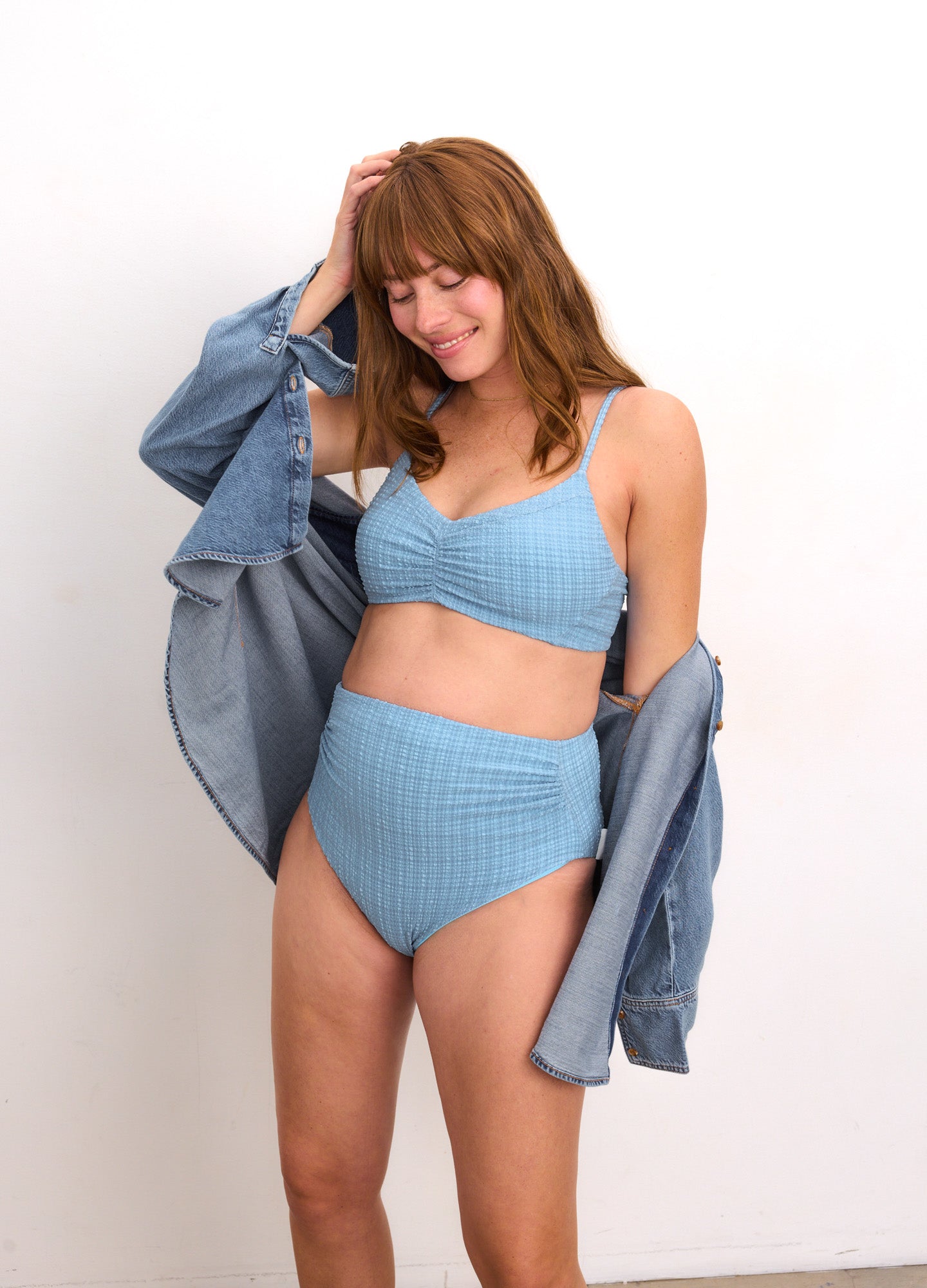 Light blue textured maternity bikini set with high-waisted bottoms and supportive top, worn by pregnant model with denim.