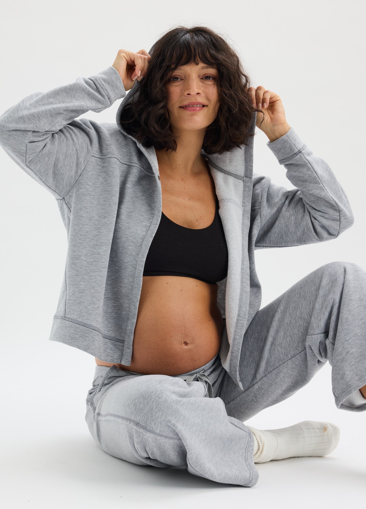 Light gray maternity hoodie with front zipper, relaxed fit, and soft fabric, styled open over black crop top.
