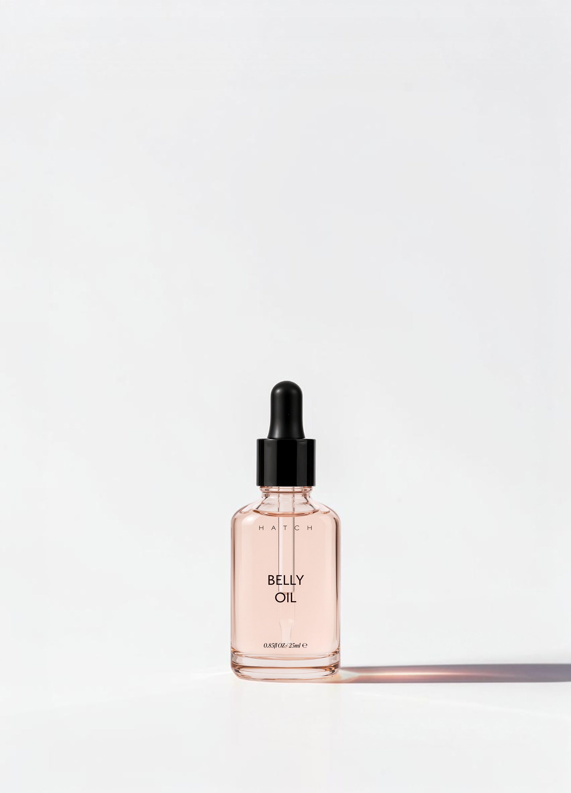 Small rectangular glass bottle of light pink belly oil with black dropper cap for maternity care.