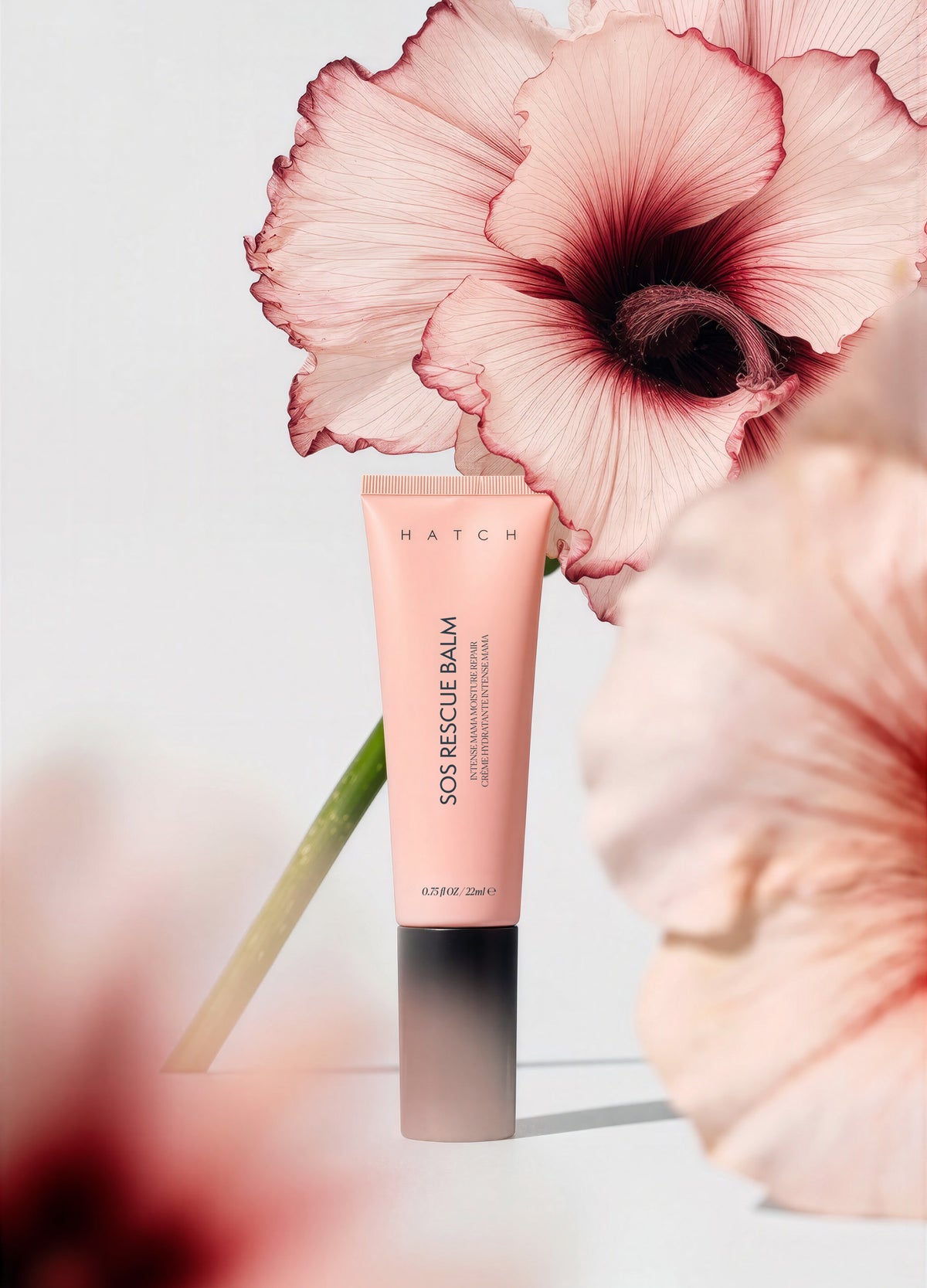 Pink tube of SOS Rescue Balm with black cap, surrounded by soft pink flowers.
